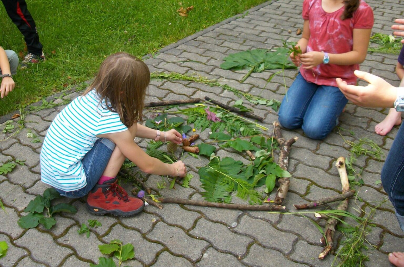 Bilder werden mit Blättern, Gräsern und Blumen auf den Boden gelegt.