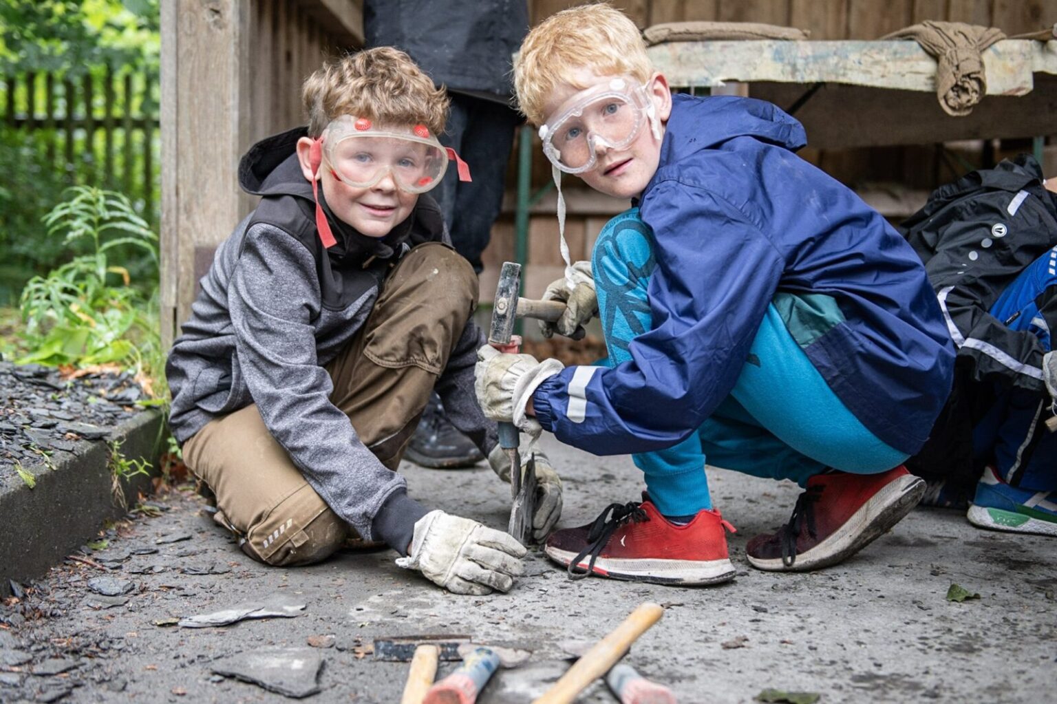 Zwei Jungen spalten eine Schifferplatte mit Hammer und Meißel