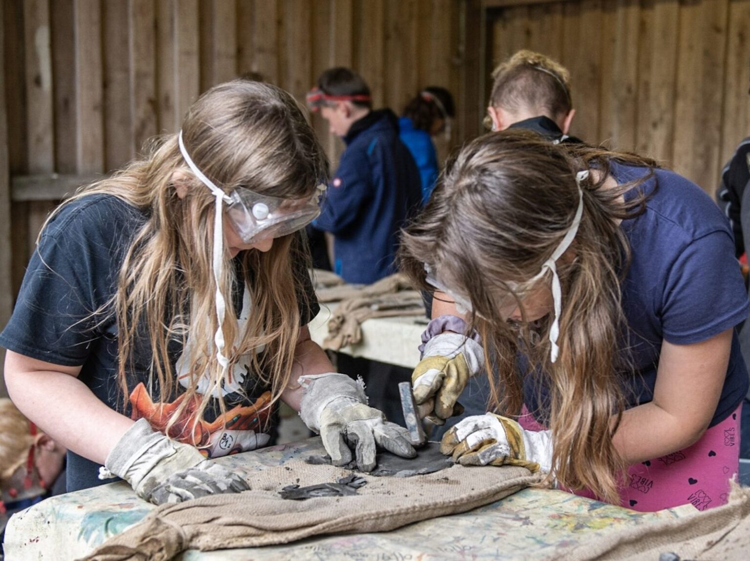 Zwei Mädchen verfeinern gerade am Tisch ihren Fossilienfund mit einem kleinen Hammer