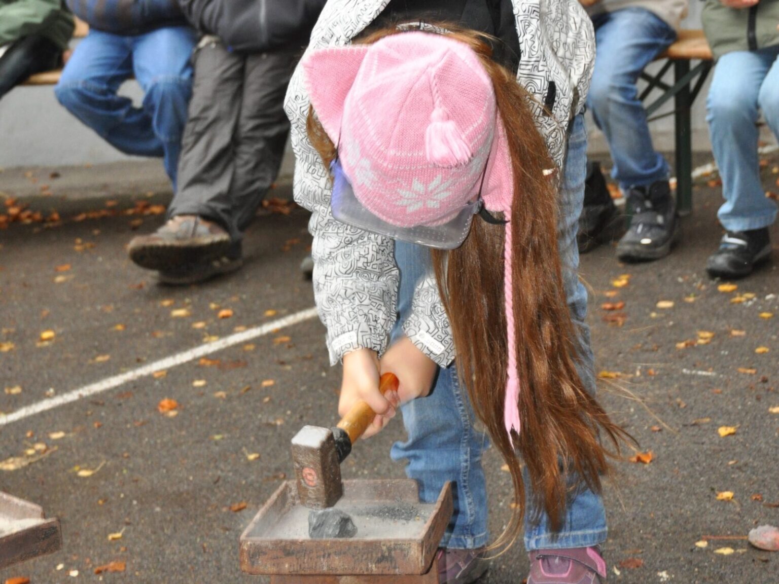 Ein Mädchen haut mit einem großen Hammer auf einen Stein