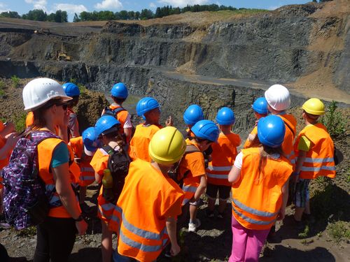 Kinder in orangenen Westen und mit Schutzhelm schauen in den Steinbruch